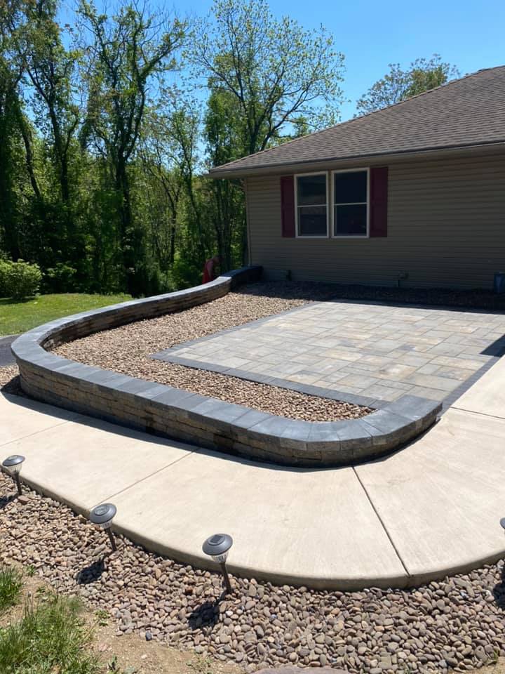 Finished paver patio framed by a curved retaining wall and concrete walkway