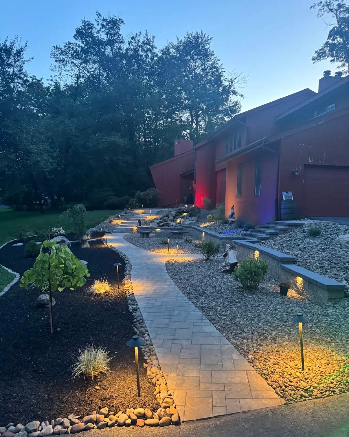 Illuminated paver walkway with tiered retaining walls and landscaped beds